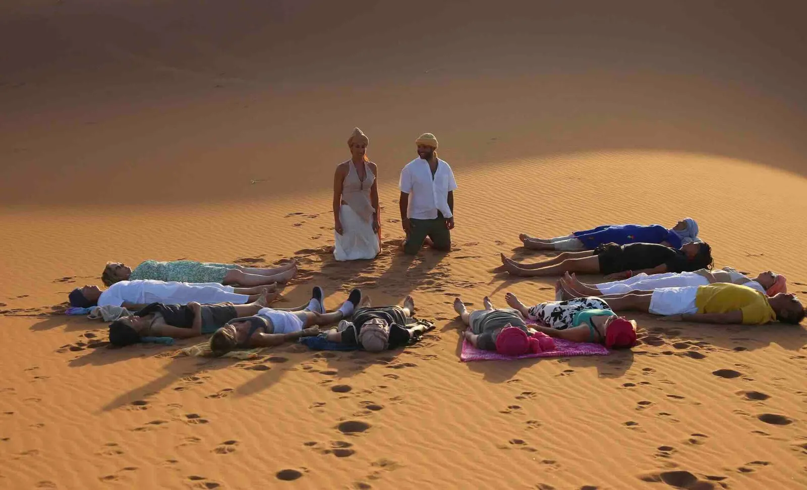 Breathwork group lying on the desert sand, guided by Melissa and Emmanuel