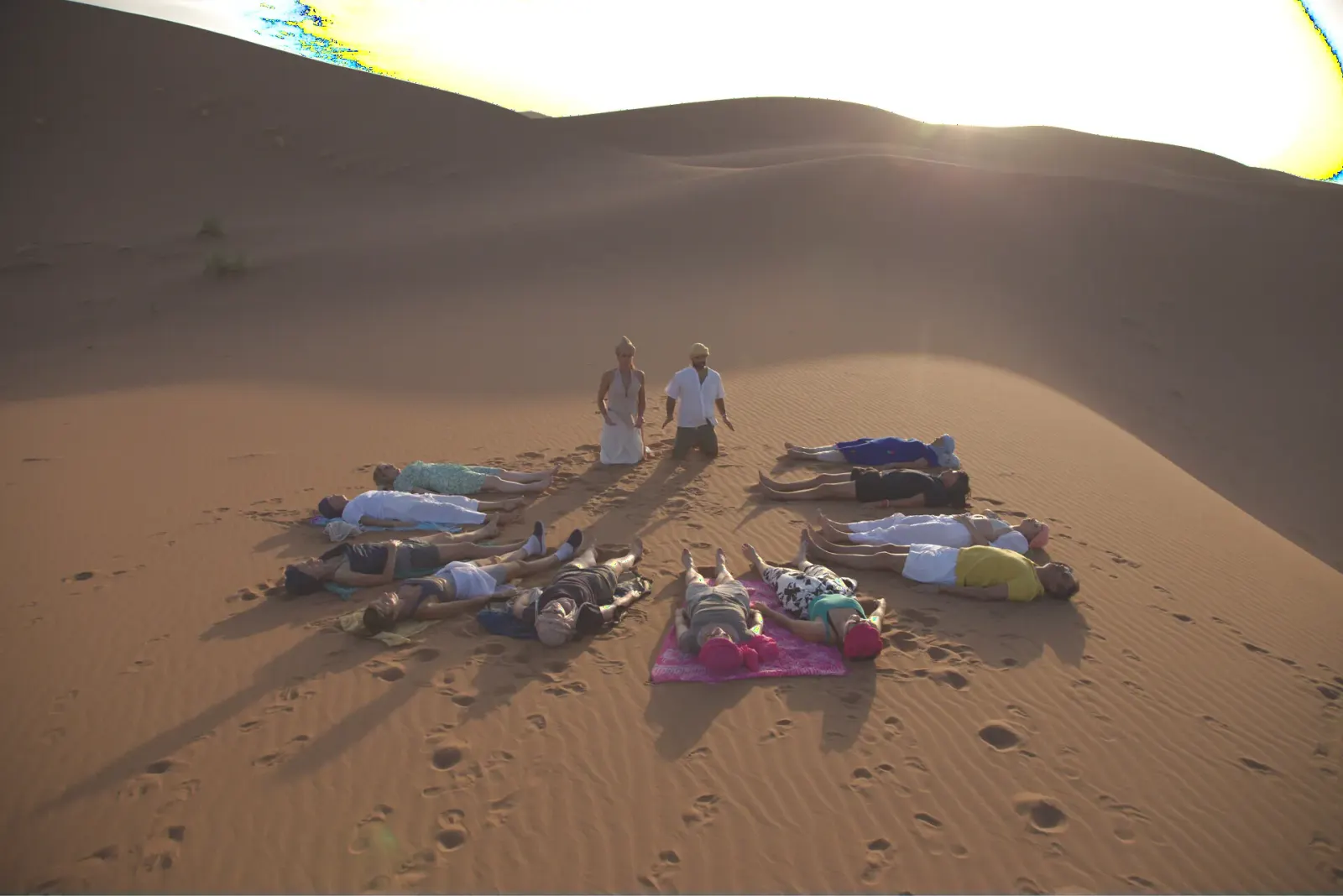 Group in a circle on the dunes during a breathwork session at sunset